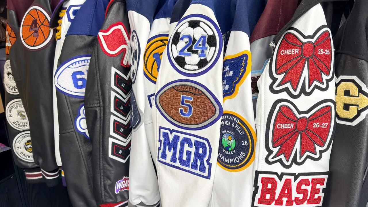 Rack of customized letterman jacket sleeves displaying basketball, soccer, football, track and field, cheer, and academic patches