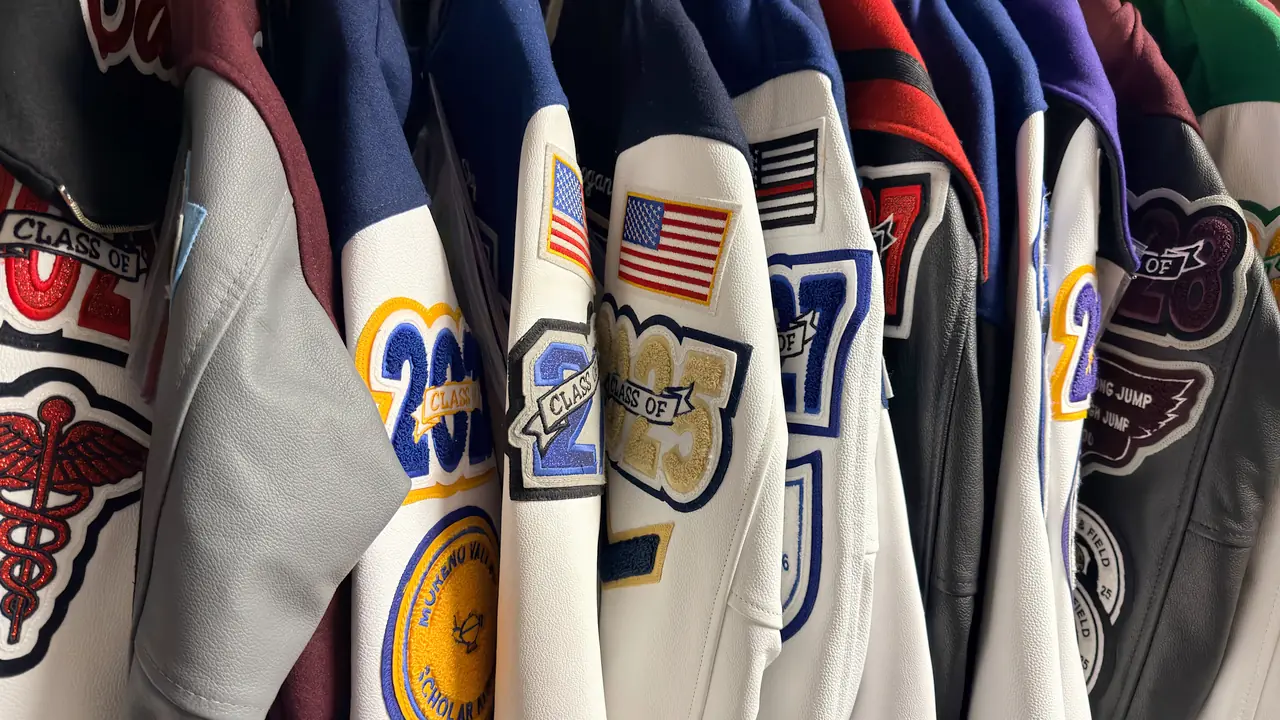 Rack of custom letterman jackets with chenille graduation-year, academic, and activity patches at Fancy Stitchin' in Moreno Valley, California